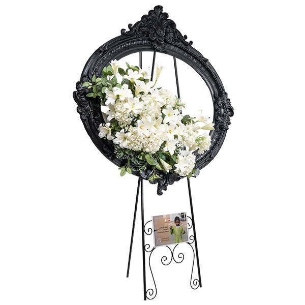 تابلوگل تسلیت مدل گلپری با قاب مشکی بیضی و گلهای سفید لیلیوم، استند اجارهای از خیریه مهربانان برای مراسم ترحیم